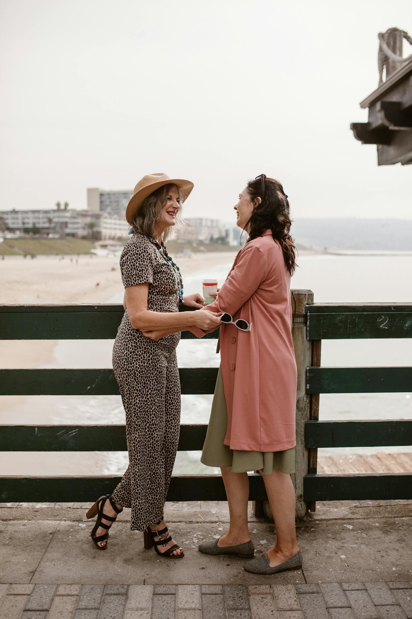 Two women sharing laughter and holding hands by the beach, embracing friendship and joy.